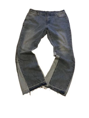 Bootcut jeans från Santo Global - Unika bootcut jeans från Santo Global i en tvättad gråblå färg. Byxorna har breda ben med insydda ljusare paneler på sidorna och råa, fransiga benslut för en edgy look. Klassisk femficksmodell och normal passform. Perfekta för dig som vill sticka ut. Nypris 499kr