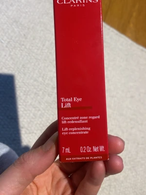 Clarins Total Eye Lift ögonkräm 7ml - Clarins Total Eye Lift är en lyxig ögonkräm i röd tub på 7 ml som jobbar med att lyfta och återfukta huden runt ögonen. Innehåller växtextrakt och har en lätt, krämig konsistens som snabbt absorberas. Perfekt för dig som vill ha piggare och slätare ögonkontur. Ny, oanvänd. 