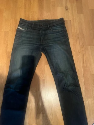 Diesel Buster jeans mörkblå W31 L32 - Säljer ett par snygga Diesel Buster jeans i mörkblå tvätt med diskreta slitningar. Klassisk femficksmodell med raka ben och stretchigt material för extra komfort. Perfekta till en avslappnad streetstil.