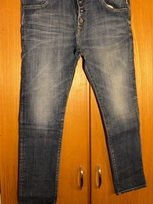 Replay jeans blå tapered herr 30 - Säljer ett par blå Replay jeans i klassisk tvätt med snygga slitningar och knappar i gylfen. Modellen har tapered passform och normal midja. Bakfickorna har dekorativa sömmar och ett rött snöre vid hällan framtill. Perfekta till vardagslooken.