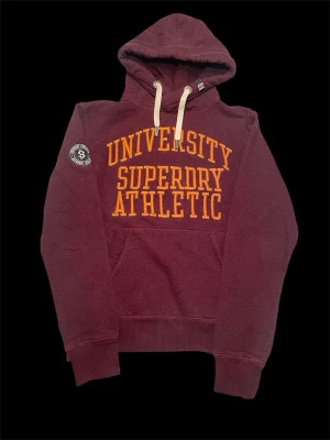 Superdry hoodie - Very stylish wine red superdry hoodie with orange embroidered text. Size L measurments are: Armpit width 56cm, Full length 65cm