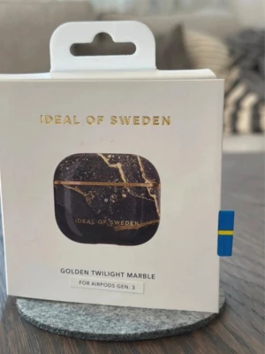 Ideal of Sweden : Golden Twilight Marble Case för AirPods Gen. 3 - Elegant och stilrent skyddsfodral i Golden Twilight Marble-design för AirPods Gen. 3. Ger fullständigt skydd och har en slimmad design. Produkten är ny i förpackning och passar perfekt för att skydda dina AirPods med stil. Aldrig använd i förpackning.