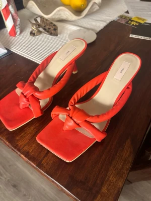 Röda klackar med knut från Nelly - Säljer ett par trendiga röda klackar  från Nelly med fyrkantig tå och låg klack. Remmarna är vadderade och har en snygg knutdetalj. Jätte fina inför sommaren när man är brun. 