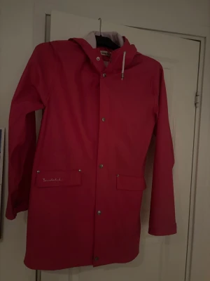 Rosa regnjacka från Bondelid - Säljer en snygg rosa regnjacka från Bondelid med huva och vita snören. Jackan har tryckknappar framtill, två stora fickor med lock och Bondelid-logga på ena fickan. Perfekt för blöta dagar och riktigt stilren look. I storlek 150/160. 