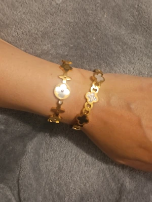 2 armband  - armband i guldton med blommotiv och detaljer, men ingen väst syns på bilderna.