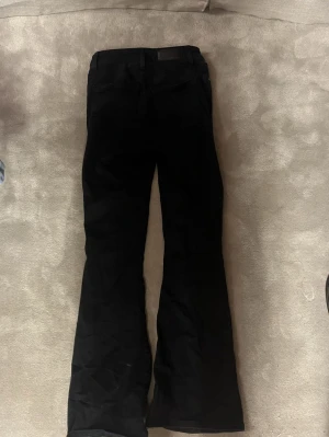 Svarta Peachy Flare jeans - Säljer ett par svarta Peachy Flare jeans med utsvängda ben och klassisk femficksdesign. Jeansen har hög midja och är tillverkade i ett stretchigt bomullsmaterial för skön passform. 