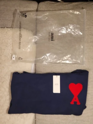 Mörkblå stickad tröja från Ami - Säljer en mörkblå stickad tröja från Ami Alexandre Mattiussi med ikonisk röd hjärtlogga och A på bröstet. Tröjan har rund hals, ribbade muddar och är långärmad. Perfekt för dig som vill ha en clean men ändå statement look.