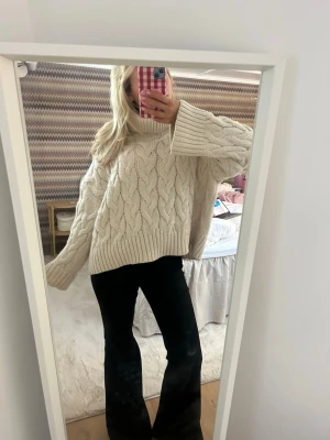 Beige kabelstickad polotröja - Säljer en oversized beige kabelstickad polotröja med breda ärmar och hög krage. Tröjan har ett grovt stickat mönster och är perfekt för kyliga dagar. Supermysig och lätt att styla med jeans eller leggings.