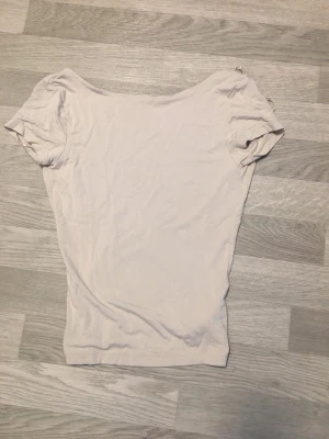 Ljusbeige topp med öppen rygg - En ljusbeige topp från Gina Tricot med korta ärmar och en djup öppen rygg. Toppen är i mjukt material och har en enkel, clean look som passar perfekt till jeans eller kjol. Snygg och basic med en twist tack vare den öppna ryggen.