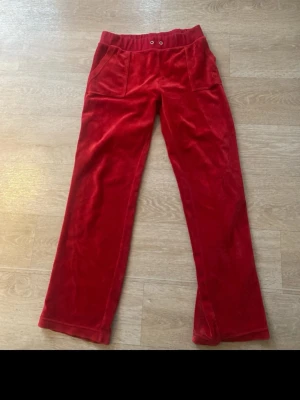 Äkta juicy couture byxor - Säljer ett par röda mjukisbyxor i mjuk sammet med resår i midjan och raka ben. Byxorna har framfickor och två bakfickor med knappdetaljer. Perfekta för en chill och avslappnad stil.