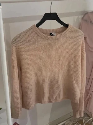 Rosa stickad tröja  - Mysig rosa stickad tröja med croppad passform och rund hals. Tröjan har långa ärmar och ribbade muddar vid halsen. Perfekt för lager på lager under höst och vinter.