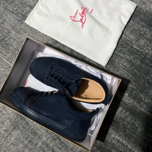 Mörkblå sneakers från Christian Louboutin - Snygga mörkblå sneakers från Christian Louboutin i mjuk mocka med klassisk röd sula och diskret logga på sidan. Skorna har rund tå, snörning och en stilren design som sticker ut med den ikoniska röda undersulan.