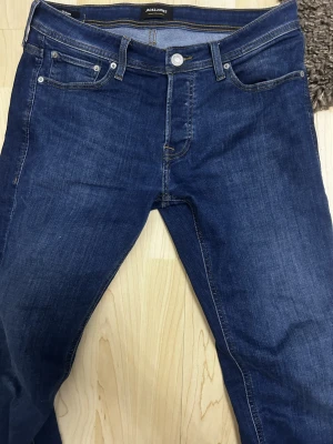 Mörkblå jeans från Jack & Jones, 32/32 - Säljer ett par klassiska mörkblå jeans från Jack & Jones i storlek 32/32. Jeansen har fem fickor, snygga kontrastsömmar och raka ben. Perfekta för dig som gillar en enkel och stilren look. Materialet är jeans och färgen är djupblå.