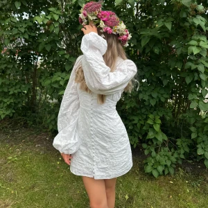 Adoore FLORENCE DRESS - Superfin vit kortklänning med broderade blommor, v-ringning och långa puffärmar. Klänningen har knappar framtill och markerad midja som ger en snygg siluett. Perfekt för somriga tillfällen , midsommar eller studenten.