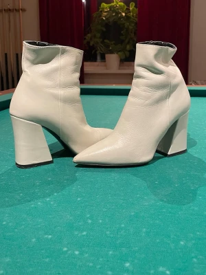 Vita boots med spetsig tå och klack - Säljer ett par vita boots från Vero Cuoio i skinn med spetsig tå och bred hög klack. Skorna har dragkedja på insidan och en stilren, minimalistisk look som passar till många outfits. Perfekta för dig som vill sticka ut med ett par trendiga boots.