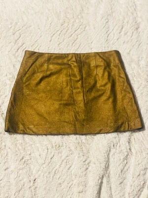 Guldig kortkjol från H&M - Säljer en glansig guldig kortkjol från H&M i storlek 34. Kjolen har en rak passform och dragkedja bak för enkel påklädning. Materialet har en metallic-finish som verkligen sticker ut och ger en cool vibe.