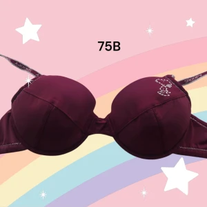 Bordeaux Snoopy bh 75B - Supersöt bordeaux bh från Snoopy med glittrigt tryck av Snoopy på ena kupan. Axelbanden har Snoopy-tryck och bh:n är tillverkad i mjuk polyamid och elastan för skön stretch. Uttagbar kuddar. Perfekt för dig som gillar roliga detaljer och vill ha något unikt under kläderna. Varan är oanvänd och kommer från ett konkurslager från 2000-talet. I många fall är prislappen kvar (se bild). Har fler annonser och bra bundlerabatt vid köp av flera.