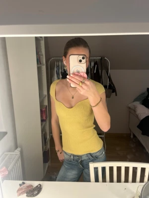 Gul ribbad topp från H&M - Supersnygg gul ribbad topp från H&M med markerad byst och korta ärmar. Toppen har en söt v-ringning och är figurnära med stretchigt material som sitter perfekt. Perfekt till jeans eller kjol för en trendig look.
