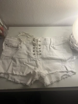 Vita low waist shorts från Billabong - Säljer ett par vita low waist shorts från Billabong i storlek 28 med snörning framtill och råa, fransiga kanter. Shortsen har slitna detaljer och klassiska fem fickor. Perfekta för sommaren.