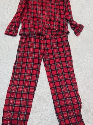 Rutig röd pyjamas från Lindex - Klassisk röd pyjamas från Lindex i mjuk bomull med rutigt mönster i svart, vitt och gult. Skjortan har knappar framtill och bröstficka, byxorna har rak passform och resår i midjan. Perfekt för mysiga kvällar hemma. Storlek 158 12-14 år. Säljer pga att jag har nya, rätt så bra skick. Meddela om du har fler frågor eller vill ha bilder.✨