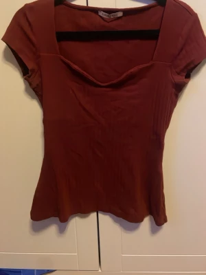 Vinröd ribbad topp - Säljer en vinröd ribbad topp med korta ärmar. Toppen är figurnära och perfekt att matcha med jeans eller kjol. Materialet är stretchigt och bekvämt, vilket gör den enkel att bära hela dagen.