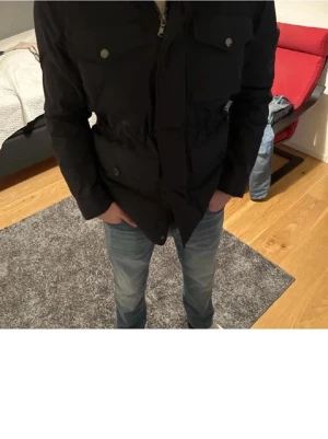 Mörkblå pufferjacka från J.Lindeberg - Pris kan diskuteras!!!                                  Säljer en mörkblå pufferjacka från J.Lindeberg med fyra fickor framtill och dragkedja. Jackan har hög krage och diskreta knappar på bröstfickorna. Tillverkad i syntetmaterial med isolering från Primaloft. Perfekt för kyliga dagar.