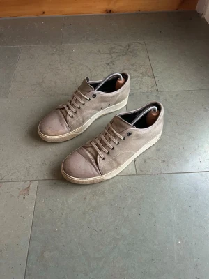 Beige sneakers från Lanvin i mocka - Säljer ett par stilrena beige sneakers från Lanvin i mjuk mocka. Skorna har rund tå, snörning och vit platt sula. Insidan är fodrad med skinn för extra komfort. Perfekta för dig som gillar minimalistisk och clean stil. Skick 5/10 storlek 43/uk9