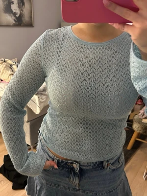 Ljusblå glittrig långärmad topp - Supersöt ljusblå långärmad topp med glittriga trådar och ett genombrutet mönster. Toppen är figurnära och har rund halsringning. Perfekt att styla med jeans eller kjol för en trendig look.