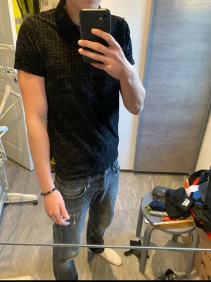 Svart mönstrad piké från Black Socks - Säljer en svart pikétröja från Black Socks i storlek XS. Tröjan har ett diskret geometriskt mönster över hela tyget, klassisk krage och knappar framtill. Perfekt för dig som gillar stilrena detaljer och vill ha något unikt i garderoben.