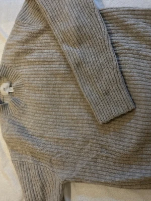 Beige ribbad stickad tröja H&M - Mysig beige stickad tröja från H&M med ribbad struktur. Tröjan har rund halsringning och långa ärmar, perfekt för kyliga dagar. Enkel och stilren design som funkar till allt.