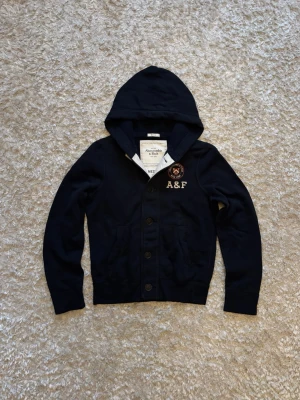 Abercrombie & Fitch blue cardigan/hoodie with buttons vintage  - Riktigt snygg o eftertraktad kofta från Abercrombie and fitch. Använd men i mycket gott skick, storlek M! Mått: Längd: 67 Bröstvidd: 55 Ärm: 70