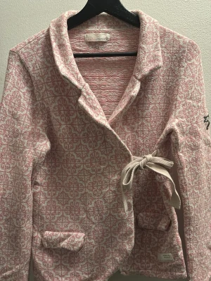 Rosa mönstrad kofta med knyt Odd Molly - Rosa och vit kofta från Odd Molly  knytband i sidan. Koftan har krage, långa ärmar och två små fickor framtill. 