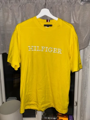 Gul t-shirt från Tommy Hilfiger - Snygg gul t-shirt från Tommy Hilfiger med stort vitt Hilfiger-tryck över bröstet. Oversized passform. Perfekt för dig som vill sticka ut med färg och enkel stil. 