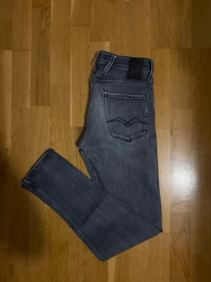 Washed Replay Anbass grå jeans, slim fit  - Säljer ett par Replay Anbass jeans i snyggt tvättad grå färg. Modellen har klassisk femficksdesign, svarta detaljer och raka ben med slim fit. Materialet är mjukt jeans-tyg med stretch för extra komfort. 