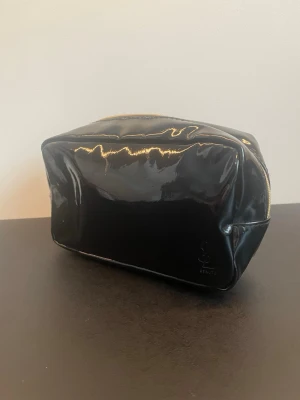 YSL beauté sminkväska - YSL - Yves Saint Laurent beauté sminkväska. Svart med gulddetaljer. Använd och kan behöva en tvätt inuti. Repig på utsidan. Liten och smidig sminkväska.