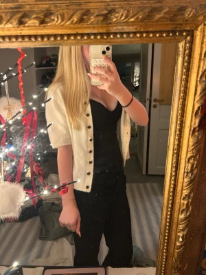 Vit kofta med kort ärm från H&M - Supersöt vit kofta från H&M med korta ärmar och rund hals. Koftan har svarta knappar framtill och är stickad i mjukt material. Perfekt att slänga över ett linne eller klänning för en chill och stilren look. Aldrig använd endast testad.