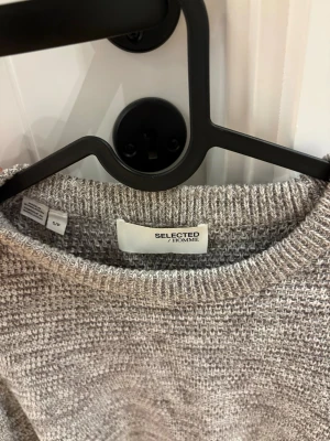Grå stickad tröja från Selected Homme - Säljer en gråmelerad stickad tröja från Selected Homme. Tröjan har rund halsringning, lång ärm och en snygg struktur i materialet. Perfekt för dig som gillar en enkel men stilren look.