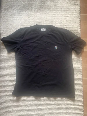 Svart t-shirt Frank Från Tunsure Copenhagen Teddy - Svart t-shirt från Frank med Copenhagen Teddy-logga på bröstet. Klassisk rund hals och korta ärmar. Tillverkad i mjuk bomull för skön känsla. Enkel och clean design med liten färgglad detalj framtill.storlek M i färgen 1st svart 1st grå och 1st marinblå 