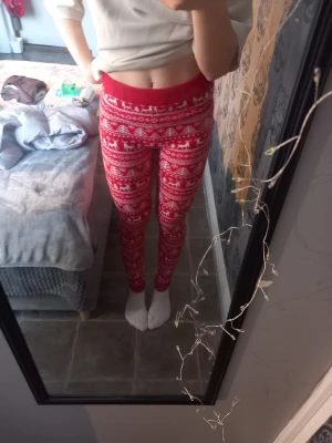 Röd julmönstrad stickad byxa Esmara - Säljer ett par röda stickade byxor från Esmara med vitt julmönster som inkluderar renar och granar. Byxorna har bred resår i midjan och är riktigt mjuka och sköna. Perfekta för mysiga vinterdagar och julfirande.