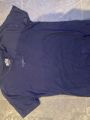Mörkblå t-shirt från Hollister - Snygg mörkblå t-shirt från Hollister Must-Have Collection med diskret logga broderad på bröstet. Klassisk rund halsringning och korta ärmar. Tillverkad i mjuk bomull som känns skön mot huden.