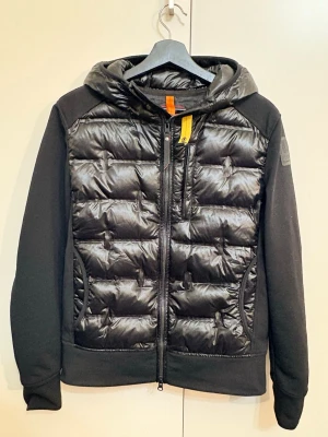 Parajumpers Gyles - Säljer en svart Parajumpers Techno Hybrid pufferjacka i storlek S. Jackan har quiltad front i blankt material, mjuka ärmar och huva. Dragkedja framtill och ikonisk PJS-patch på ärmen. Perfekt för dig som vill ha en sportig och clean look.