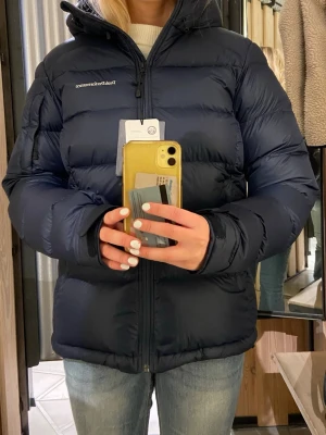 Mörkblå dunjacka Peak Performance - Säljer en mörkblå dunjacka från Peak Performance med huva och dragkedja framtill. Jackan är använd flertal gånger men har inga defekter någon stans. 