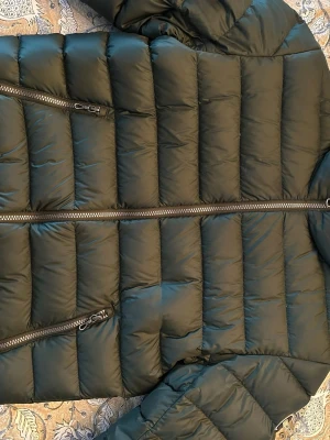 Grön  pufferjacka från Colmar - Säljer en grön pufferjacka från Colmar med snygga horisontella sömmar och två praktiska fickor med dragkedja. Jackan har en rund Colmar-logga på ärmen och är tillverkad i polyester. Perfekt för kalla dagar och har en modern, normal passform.