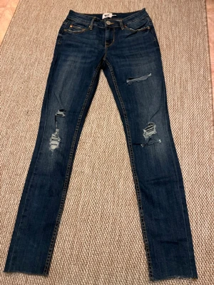 Mörkblå skinny jeans med slitningar - Säljer ett par mörkblå skinny jeans med snygga slitningar på både lår och knän. Skulle säga att det är Low-mid waist! Jeansens hela längd är 90! Aldrig använt😊