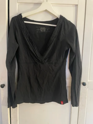 Svart omlottopp från edc - Säljer en svart omlottopp från edc med lång ärm och djup v-ringning. Toppen har en snygg ribbad kant längs ringningen.