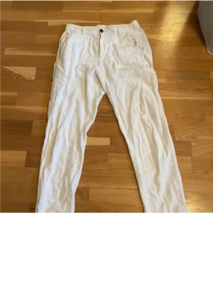 Vita linnebyxor med avslappnad passform - Säljer ett par vita linnebyxor med normal passform och elastisk midja bak. Byxorna har raka ben, sidofickor fram och bakfickor med knapp. Perfekta för varma dagar och ger en clean och fräsch look.