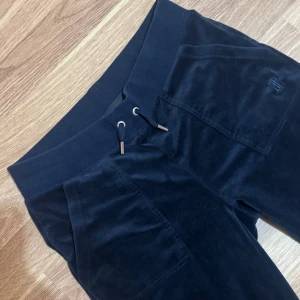 Mörkblåa Juicy Couture XS - Säljer ett par mörkblåa mjukisbyxor från Juicy Couture i storlek XS. Byxorna har snörning i midjan, raka ben och praktiska fickor både fram och bak med snygga detaljer. Mjukt velourmaterial som är superbekvämt och ger en cool vibe. Säljer pga att jag knappt använder dom längre, priset går att diskutera💞