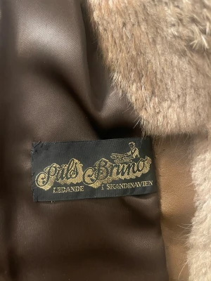 Brun pälsjacka från Päls Bruno - Snygg vintage pälsjacka från Päls Bruno i olika bruna nyanser. Jackan har klassisk rak passform, lång ärm och mjukt foder. Pälsen är tät och fluffig, perfekt för kalla dagar. Märke broderat på insidan. Riktigt statement-plagg för dig som vill sticka ut.