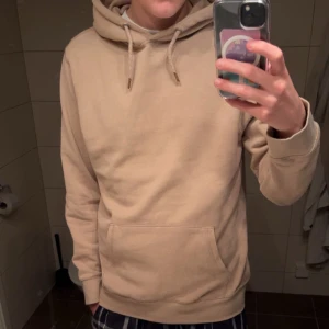 Mörkbrun hoodie från 157 med huva - Säljer en stilren mörkbrun hoodie från 157 med klassisk känguruficka och justerbar huva med snören. Tröjan har långa ärmar och ribbade muddar. Perfekt för chill dagar och enkel att matcha med jeans eller mjukisbyxor. Har använts en del men bra skick på den ändå. Hör av er om ni har frågor!