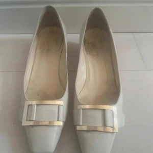 Vita klackskor med gulddetalj - Snygga vita klacksor från Vero Cuoio, tillverkade i Italien. Tillverkade i skinn för en lyxig känsla. Perfekt för dig som gillar klassisk och stilren design. Skavanker syns på sista två bilderna, däremot syns dom ej i verkligheten lika mycket. 